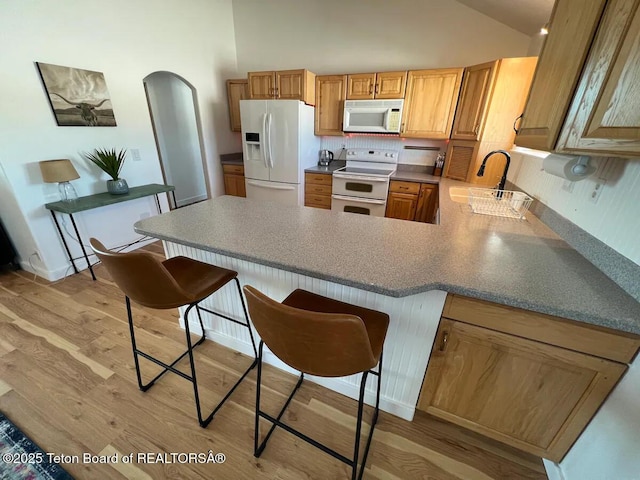 kitchen featuring a kitchen bar, sink, light hardwood / wood-style flooring, kitchen peninsula, and white appliances