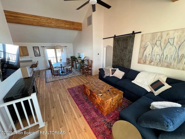 living room featuring beam ceiling, high vaulted ceiling, ceiling fan, a barn door, and light hardwood / wood-style floors