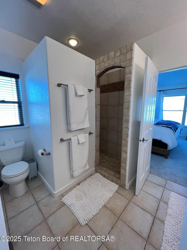 bathroom featuring toilet, a healthy amount of sunlight, a textured ceiling, and tiled shower