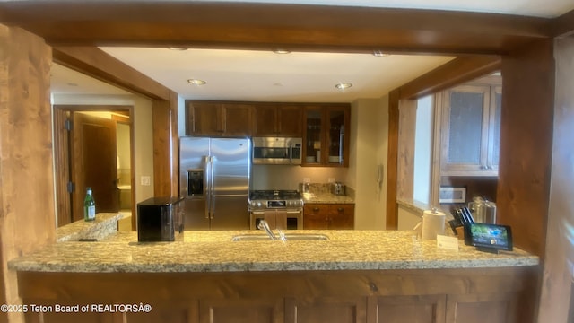 kitchen with stainless steel appliances, light stone countertops, and sink