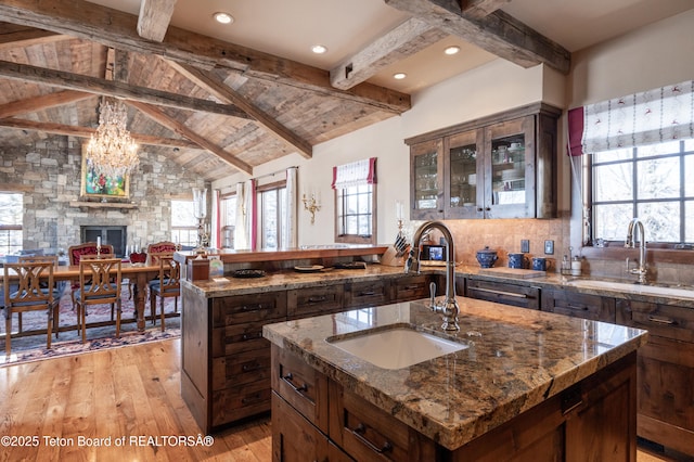 kitchen with beamed ceiling, dark stone countertops, sink, and a center island with sink