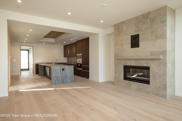 kitchen with dark brown cabinetry, light hardwood / wood-style flooring, a kitchen breakfast bar, an island with sink, and a fireplace