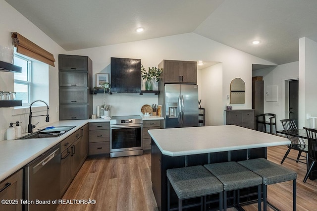 kitchen with a kitchen bar, sink, vaulted ceiling, stainless steel appliances, and range hood