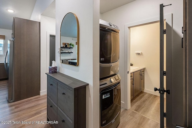 clothes washing area featuring stacked washer / drying machine and light hardwood / wood-style flooring