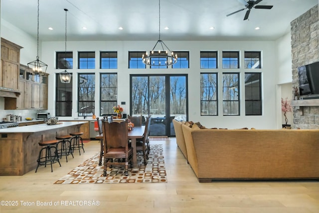 dining room with ceiling fan with notable chandelier, a towering ceiling, and light wood-type flooring