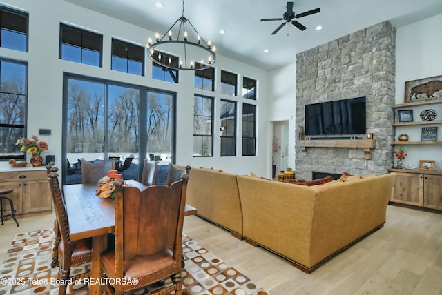 living room featuring a towering ceiling, ceiling fan with notable chandelier, a fireplace, and light wood-type flooring