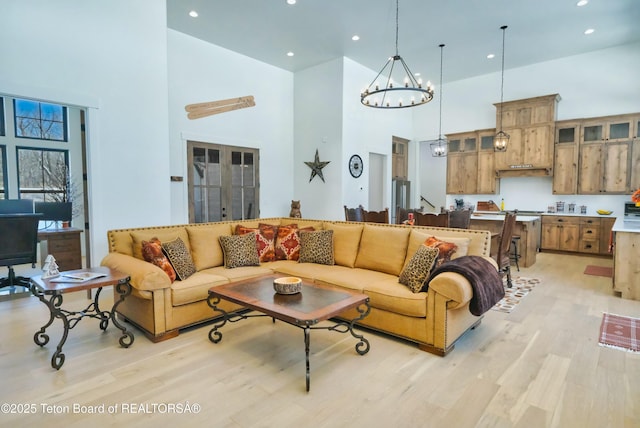 living room with french doors, a towering ceiling, a notable chandelier, and light hardwood / wood-style flooring