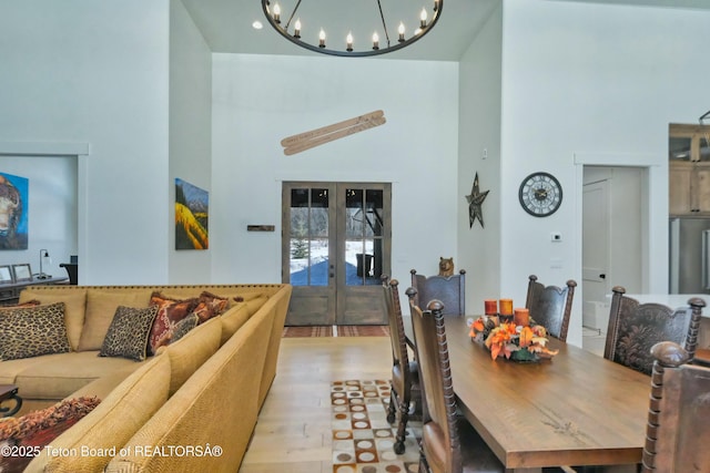 dining space with light wood-type flooring, french doors, a chandelier, and a high ceiling