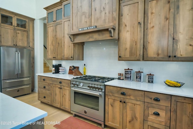 kitchen with high quality appliances, tasteful backsplash, exhaust hood, and light hardwood / wood-style flooring