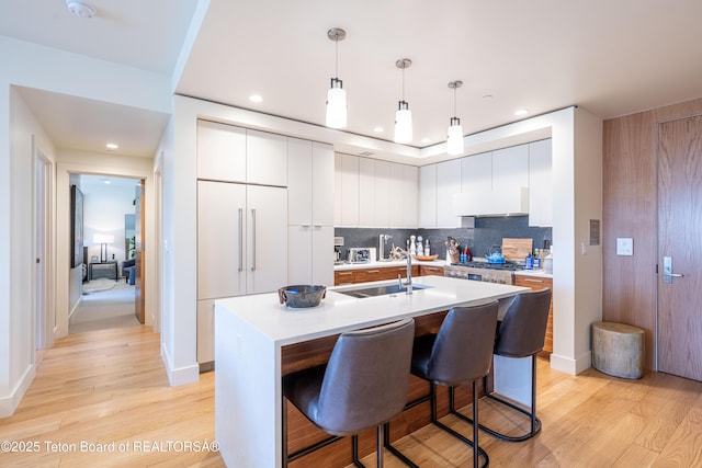 kitchen with hanging light fixtures, white cabinetry, an island with sink, and light hardwood / wood-style flooring