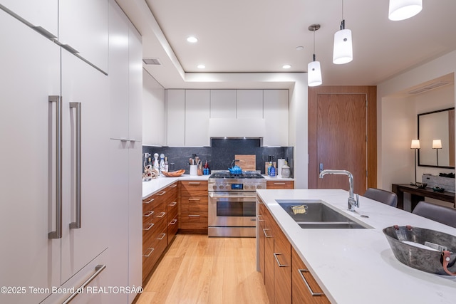 kitchen featuring sink, premium appliances, light stone countertops, white cabinets, and decorative light fixtures