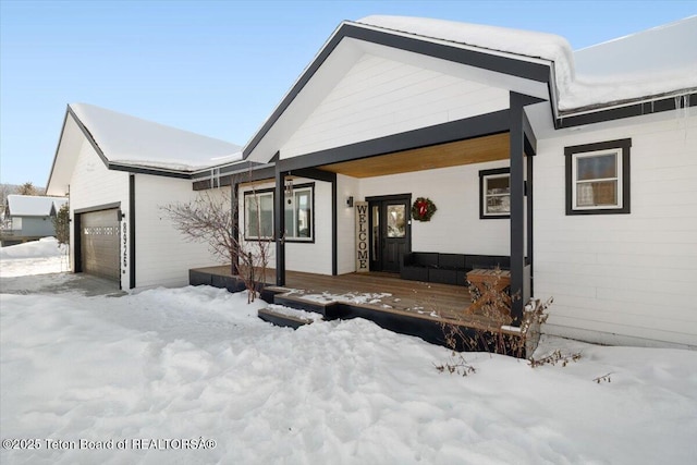 snow covered property with a garage and covered porch