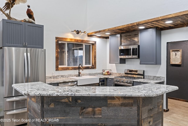 kitchen with stainless steel appliances, light stone countertops, sink, and kitchen peninsula