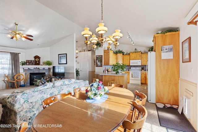 dining space with ceiling fan with notable chandelier, lofted ceiling, light carpet, and a fireplace