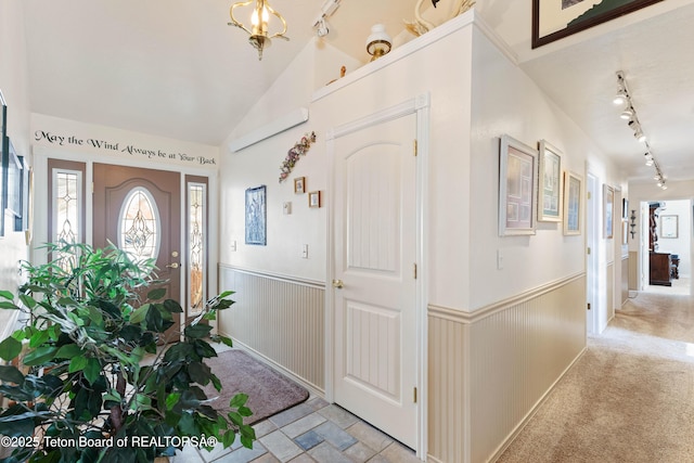 foyer entrance featuring vaulted ceiling, light colored carpet, and rail lighting