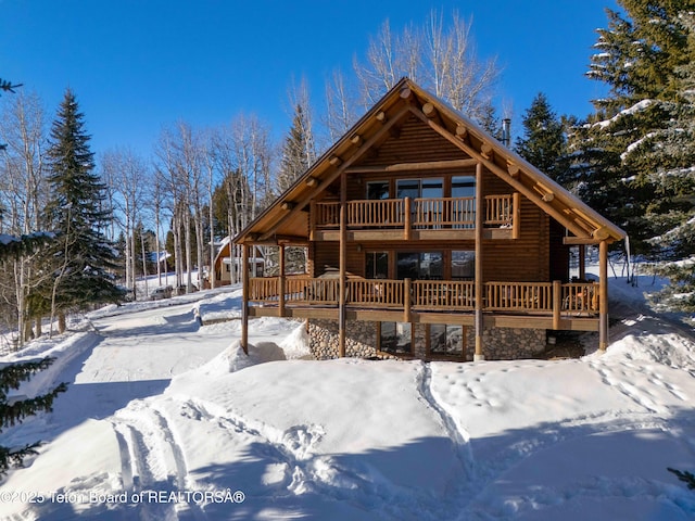 snow covered rear of property featuring a wooden deck and a balcony