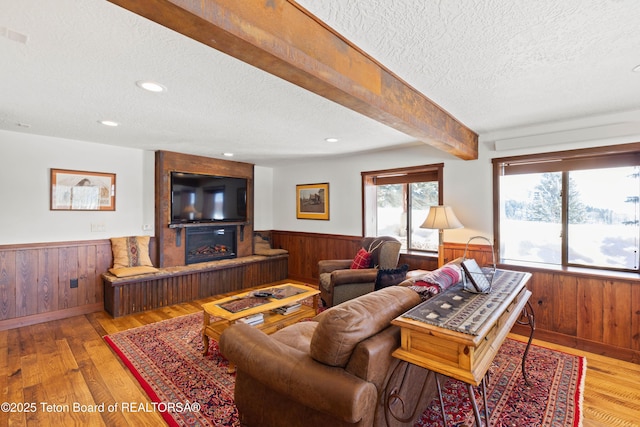 living room with wooden walls, a large fireplace, light hardwood / wood-style floors, a textured ceiling, and beam ceiling