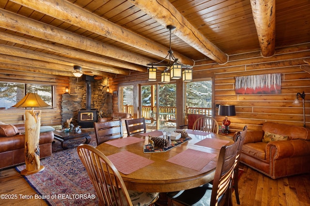 dining area featuring log walls, wood-type flooring, a wood stove, and wooden ceiling