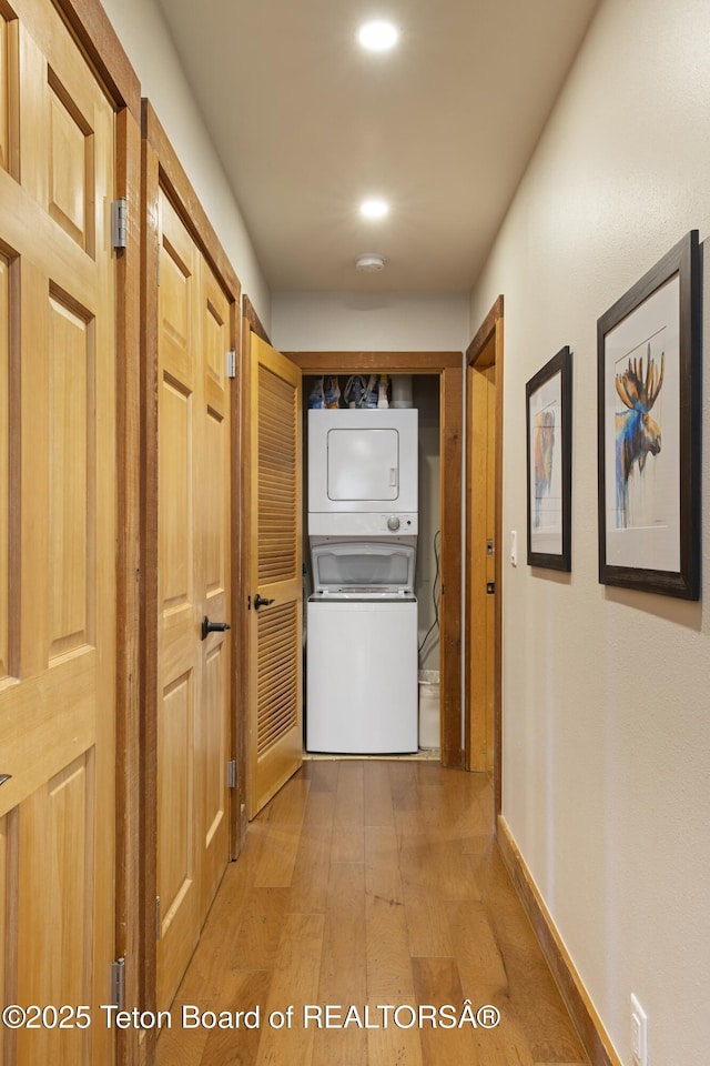 hallway with stacked washing maching and dryer and light hardwood / wood-style flooring