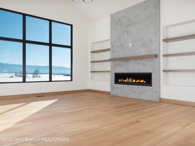 unfurnished living room with high vaulted ceiling, a large fireplace, a mountain view, built in features, and hardwood / wood-style flooring