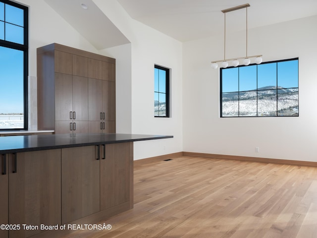 kitchen with lofted ceiling, a breakfast bar area, hanging light fixtures, light hardwood / wood-style floors, and dark brown cabinets