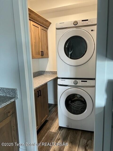 laundry room with cabinets, stacked washer / drying machine, and dark hardwood / wood-style flooring