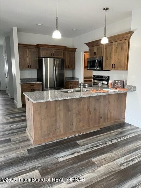 kitchen with sink, appliances with stainless steel finishes, light stone countertops, dark hardwood / wood-style flooring, and decorative light fixtures