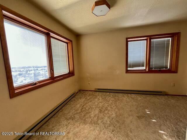 unfurnished room featuring a baseboard heating unit, a textured ceiling, and carpet flooring