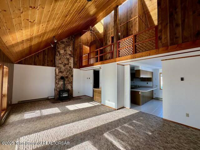 unfurnished living room with high vaulted ceiling, a wood stove, light carpet, and wood ceiling