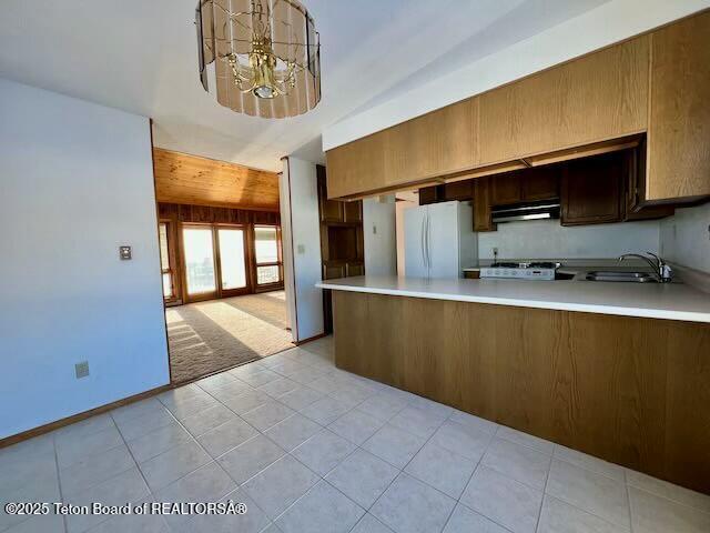 kitchen with sink, light tile patterned floors, a notable chandelier, kitchen peninsula, and white fridge