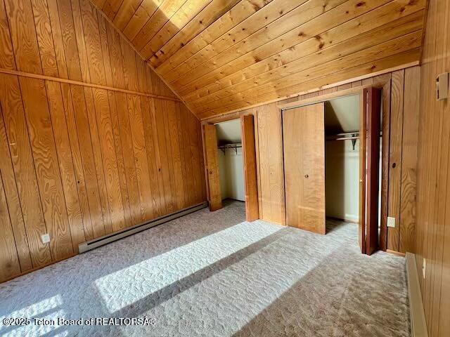 unfurnished bedroom with lofted ceiling, wood ceiling, two closets, a baseboard radiator, and wood walls