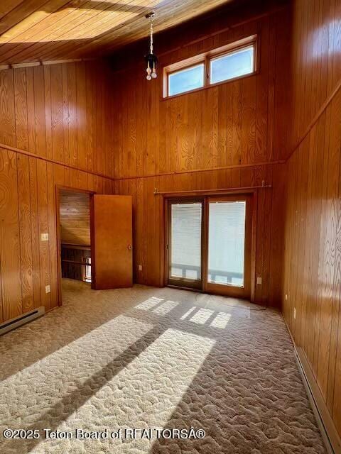 unfurnished room with baseboard heating, a towering ceiling, a notable chandelier, wooden ceiling, and wood walls