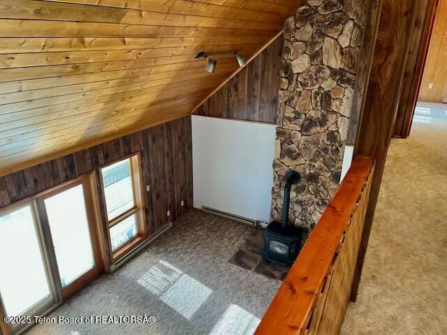 bonus room with wood walls, wood ceiling, a wood stove, baseboard heating, and light colored carpet