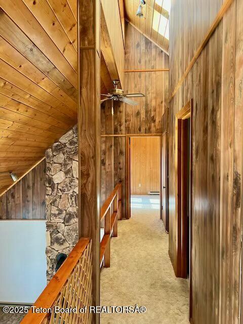 hall featuring light carpet, wooden ceiling, high vaulted ceiling, and wood walls