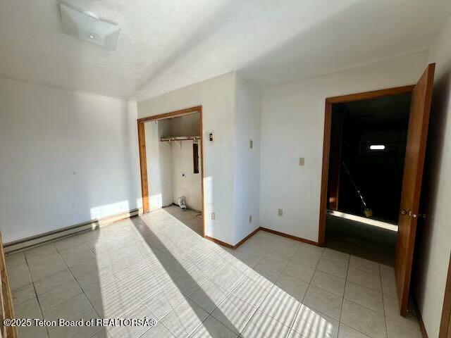 tiled empty room with lofted ceiling and baseboard heating