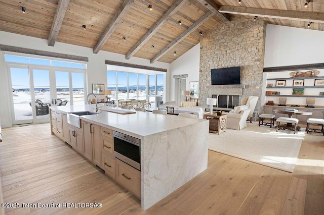 kitchen with sink, wood ceiling, light hardwood / wood-style flooring, a kitchen island with sink, and a fireplace