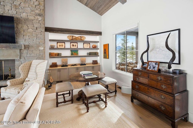 sitting room featuring high vaulted ceiling, a stone fireplace, and light hardwood / wood-style floors