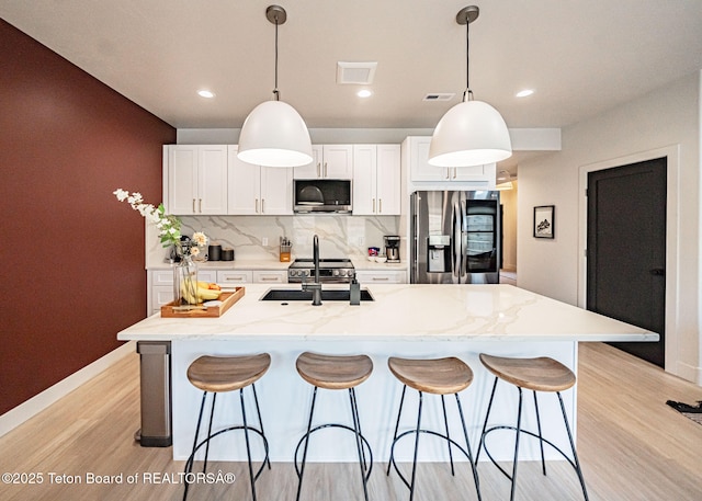 kitchen with appliances with stainless steel finishes, a kitchen island with sink, and decorative light fixtures