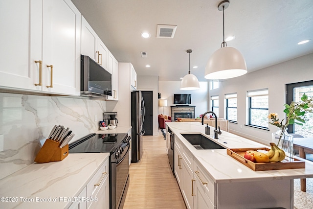 kitchen featuring sink, stainless steel fridge, white cabinets, hanging light fixtures, and black / electric stove