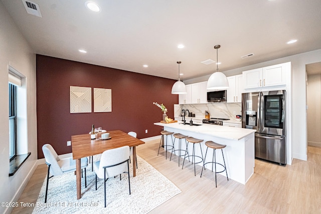 kitchen with sink, decorative light fixtures, stainless steel appliances, a kitchen island with sink, and white cabinets