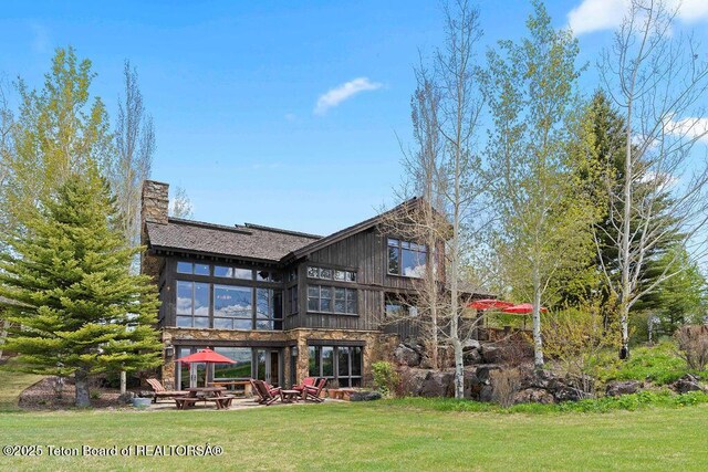 380 Cottongrass Rd, Driggs, ID 83422 - rear view of property with a yard, a patio, a fire pit, a chimney, and stone siding