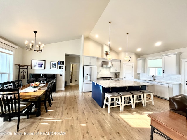 kitchen with wall chimney exhaust hood, pendant lighting, white appliances, a large island, and white cabinets