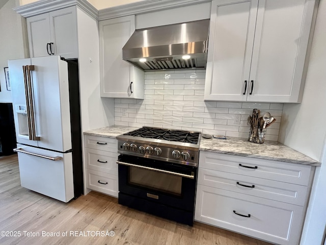 kitchen with high quality appliances, ventilation hood, light stone countertops, white cabinets, and light wood-type flooring