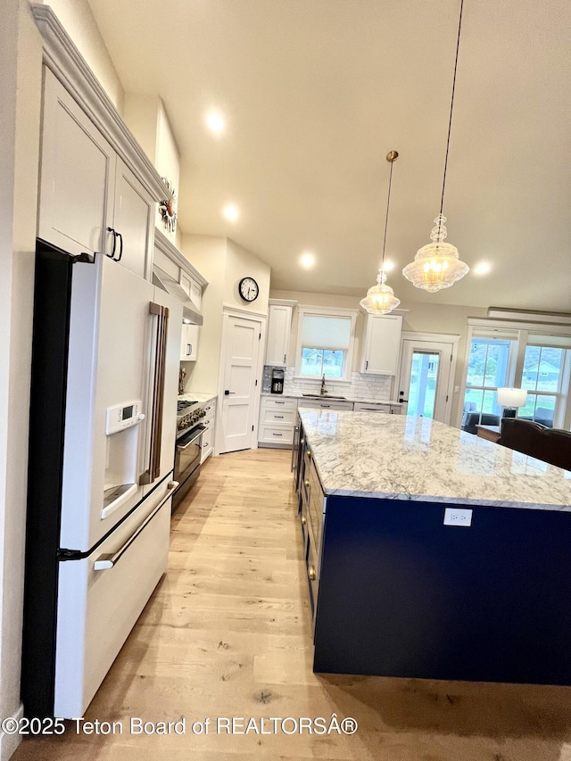 kitchen featuring a kitchen island, pendant lighting, high quality appliances, sink, and light stone counters