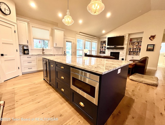 kitchen with white cabinetry, a center island, hanging light fixtures, stainless steel microwave, and a fireplace