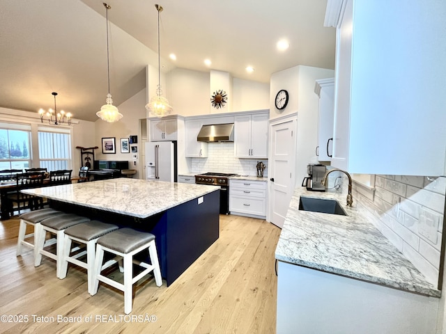 kitchen featuring white cabinetry, high quality appliances, light stone counters, a kitchen island, and wall chimney exhaust hood