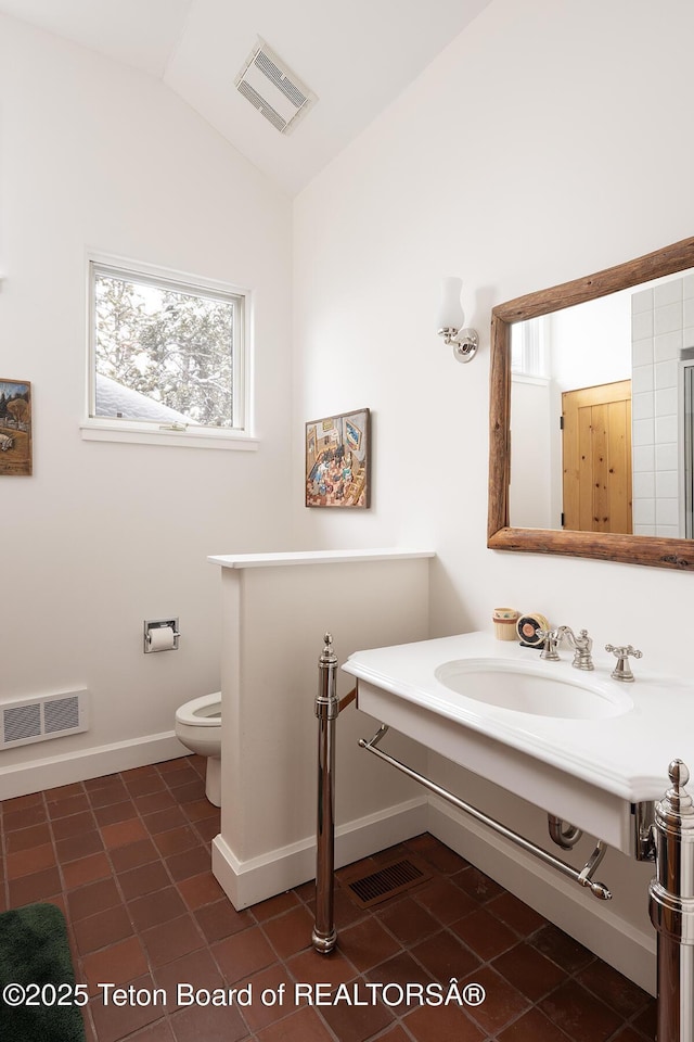 bathroom with toilet, visible vents, vaulted ceiling, and a sink