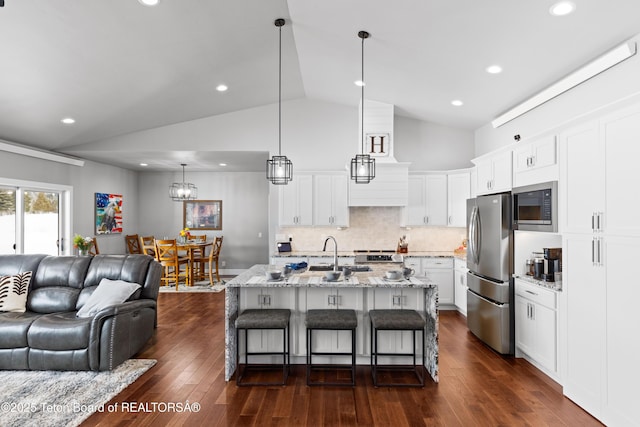 kitchen with white cabinets, hanging light fixtures, a kitchen island with sink, light stone counters, and stainless steel appliances