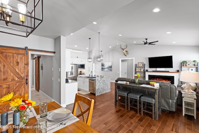 dining room featuring sink, ceiling fan, dark hardwood / wood-style flooring, vaulted ceiling, and a barn door