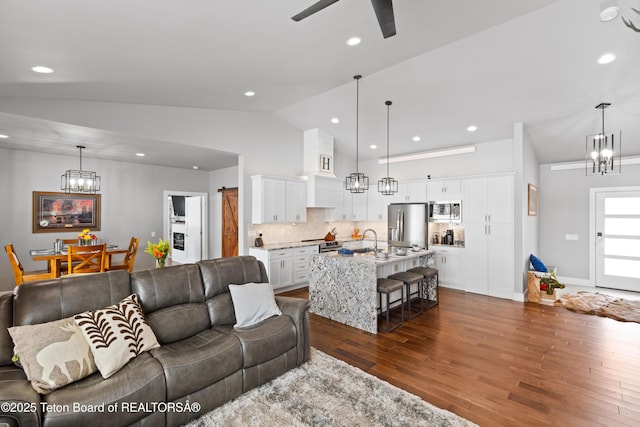 living room with ceiling fan with notable chandelier, sink, dark hardwood / wood-style flooring, and vaulted ceiling